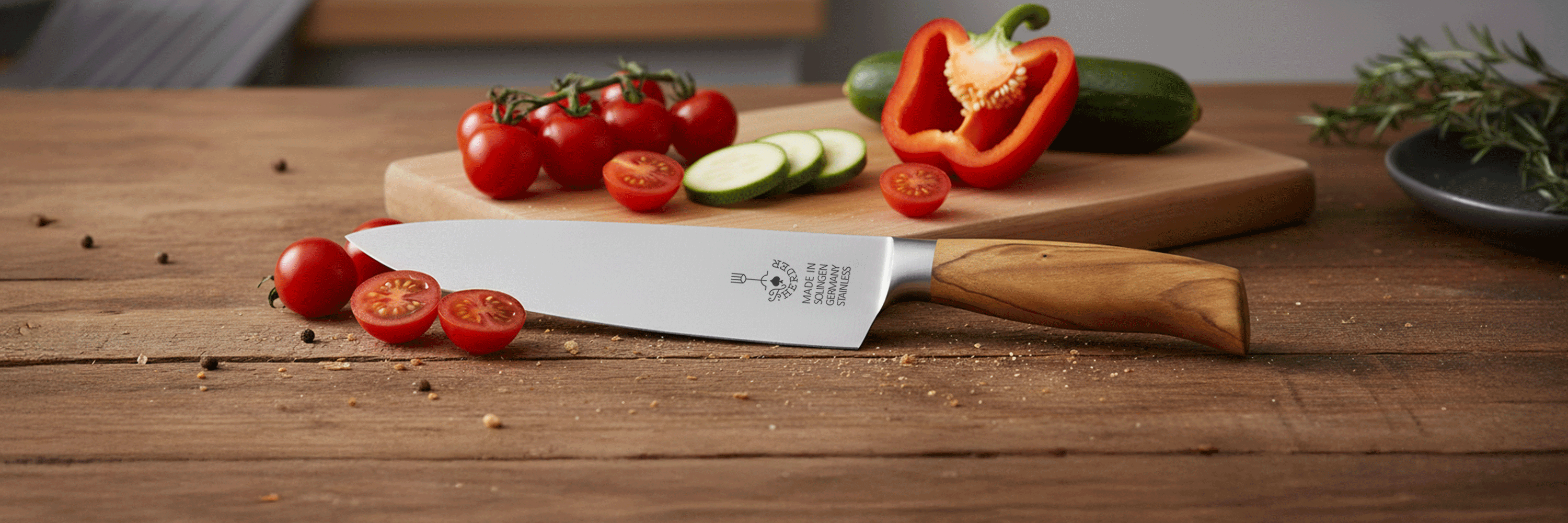 Hochwertiges Solinger Kochmesser mit Edelstahlklinge und Olivenholzgriff, ideal zum Schneiden von Gemüse wie Tomaten, Gurken und Paprika.  
